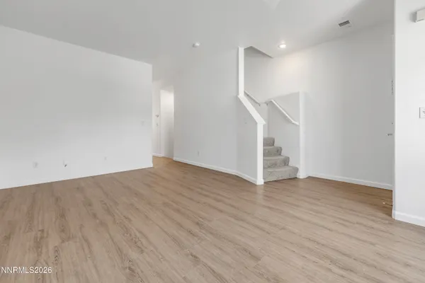 a view of an empty room with wooden floor and stairs