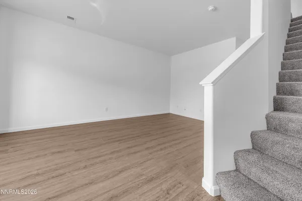 a view of an empty room with wooden floor and stairs