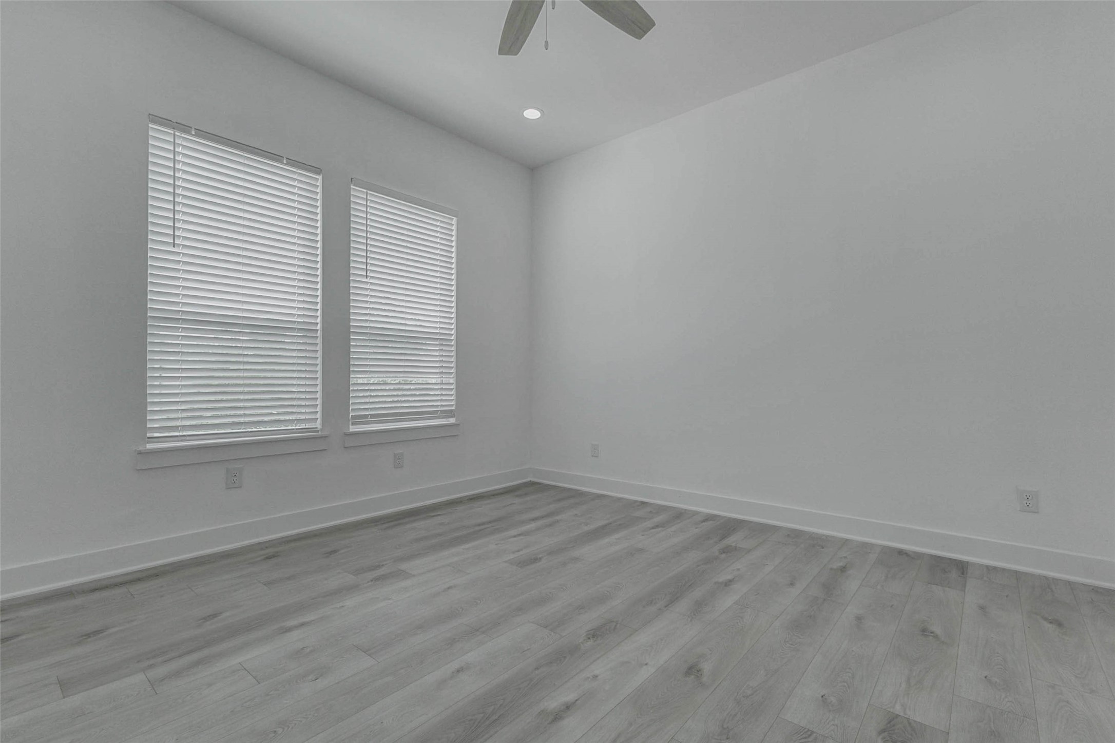 5705 Elysium Street Houston, TX 77091 - Photo 17 of 22 Bright primary bedroom with two tall windows, white blinds, ceiling fan, recessed lighting, and light wood-look flooring. The room’s high ceilings, neutral walls, and open floor space create a comfortable private retreat with a fresh modern look and flexible layout options for bedroom furniture or decor.