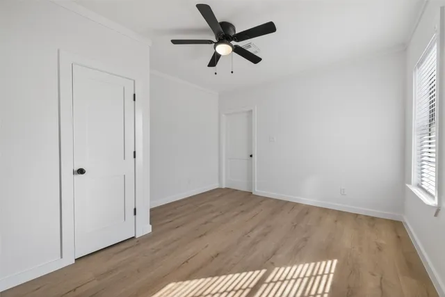 an empty room with wooden floor fan and windows