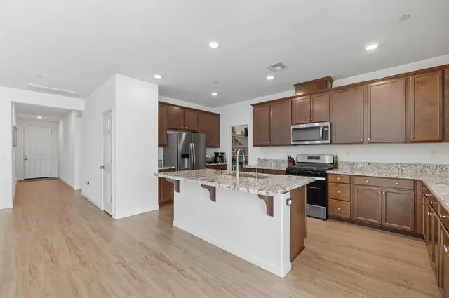 a kitchen with stainless steel appliances granite countertop a stove top oven a sink dishwasher a refrigerator and a oven with wooden floor