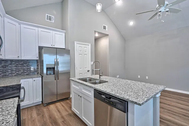 a kitchen with stainless steel appliances granite countertop a sink dishwasher a refrigerator and a stove with wooden floor