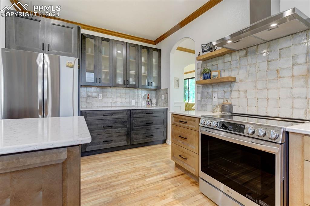 20880 Scott Road Calhan, CO 80808 - Photo 10 of 50 Kitchen with wall chimney range hood, decorative backsplash, light wood-type flooring, crown molding, and stainless steel appliances