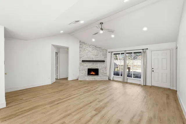a view of an empty room with wooden floor fireplace and a window