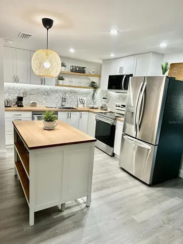 a kitchen with stainless steel appliances granite countertop a sink a stove a refrigerator and island with wooden floor