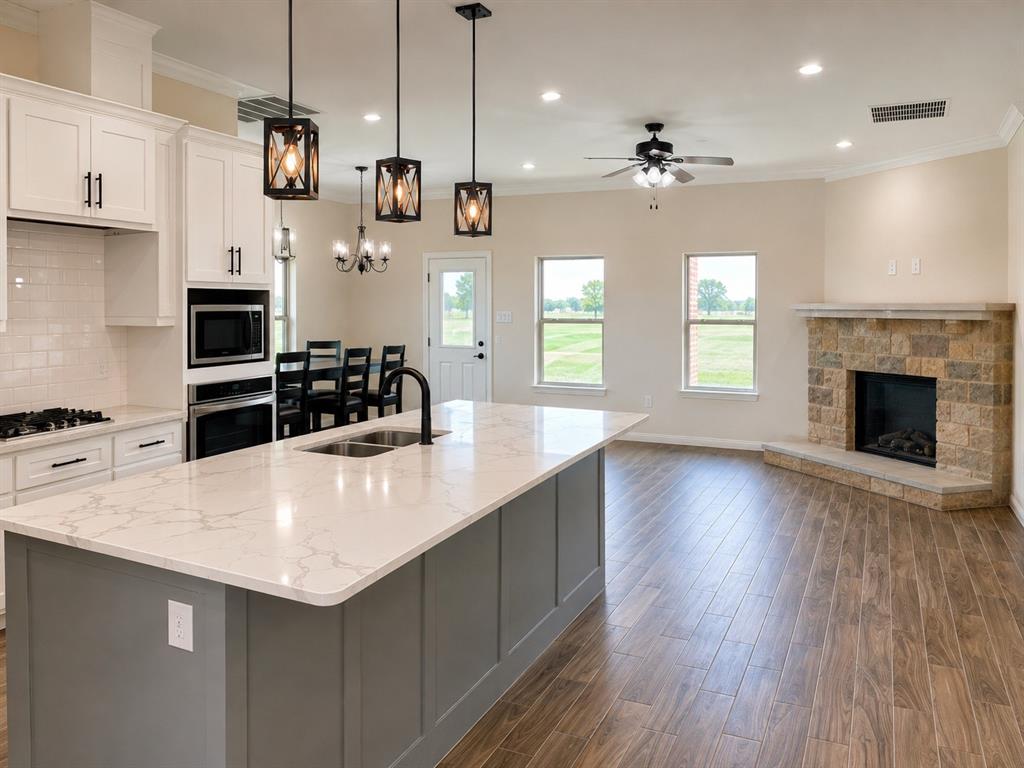 8008 County Road 1058 Rice, TX 75155 - Photo 3 of 12 Spacious kitchen with a large island, white cabinetry, integrated stainless steel appliances, and wood-finish flooring extending to a living area with a stone fireplace