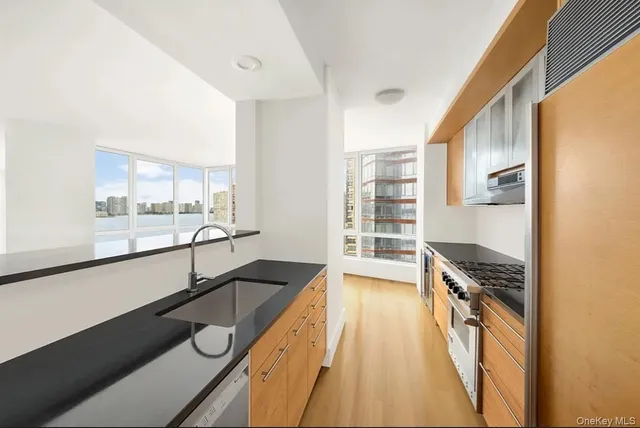 a view of a kitchen with kitchen island a counter top space a sink wooden floor and stainless steel appliances