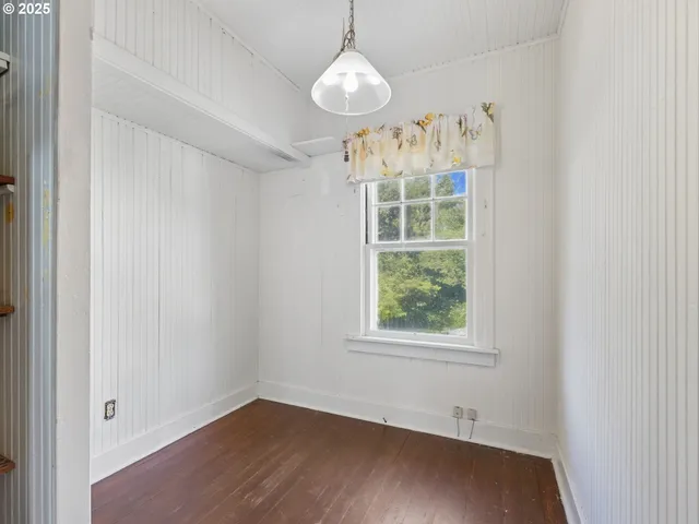 an empty room with wooden floor exposed radiator and a window