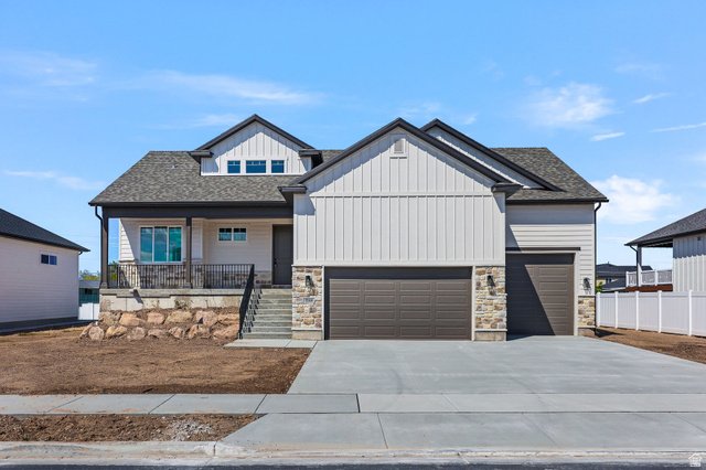 Modern Farmhouse exterior featuring a covered front porch, a two-car garage, stone accents, and vertical siding