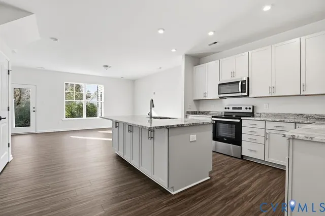 a kitchen with stainless steel appliances granite countertop a stove top oven a sink a refrigerator with white cabinets and wooden floor