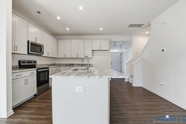a kitchen with kitchen island granite countertop a sink a stove oven and white cabinets