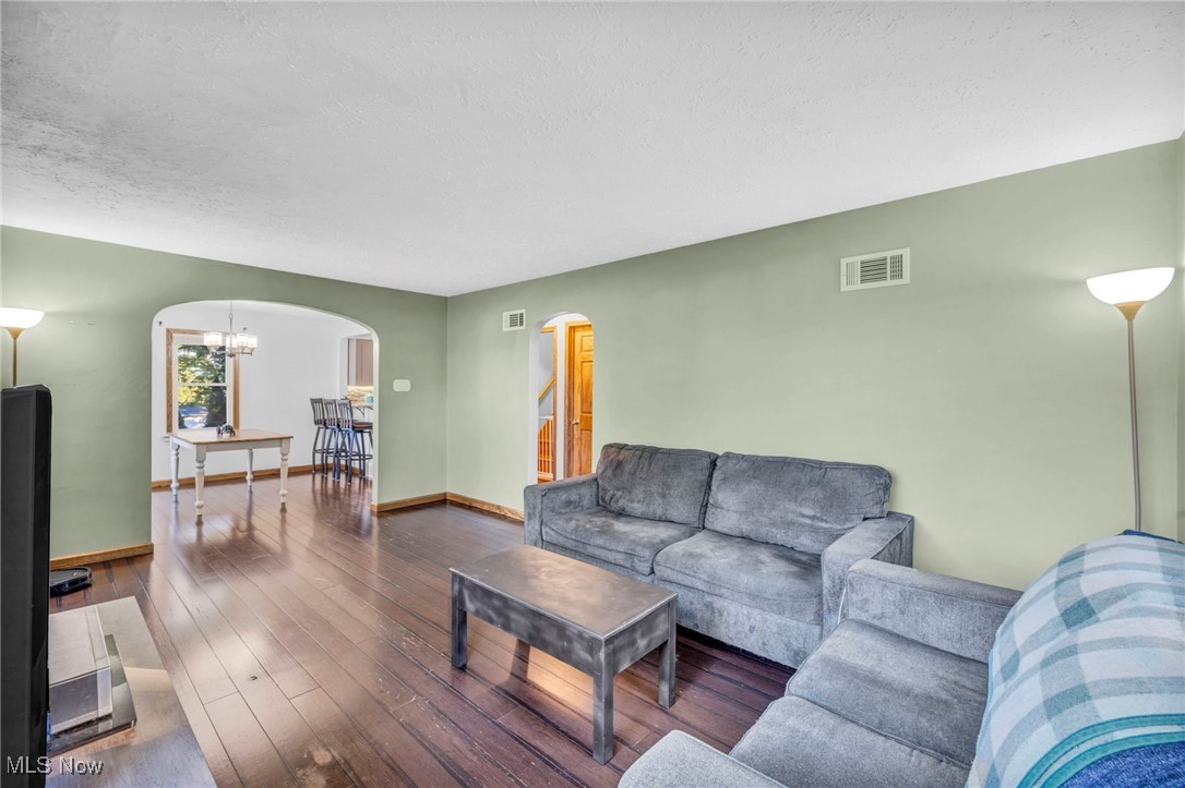 Living area with arched walkways, a textured ceiling, wood-type flooring, a chandelier, and stairway