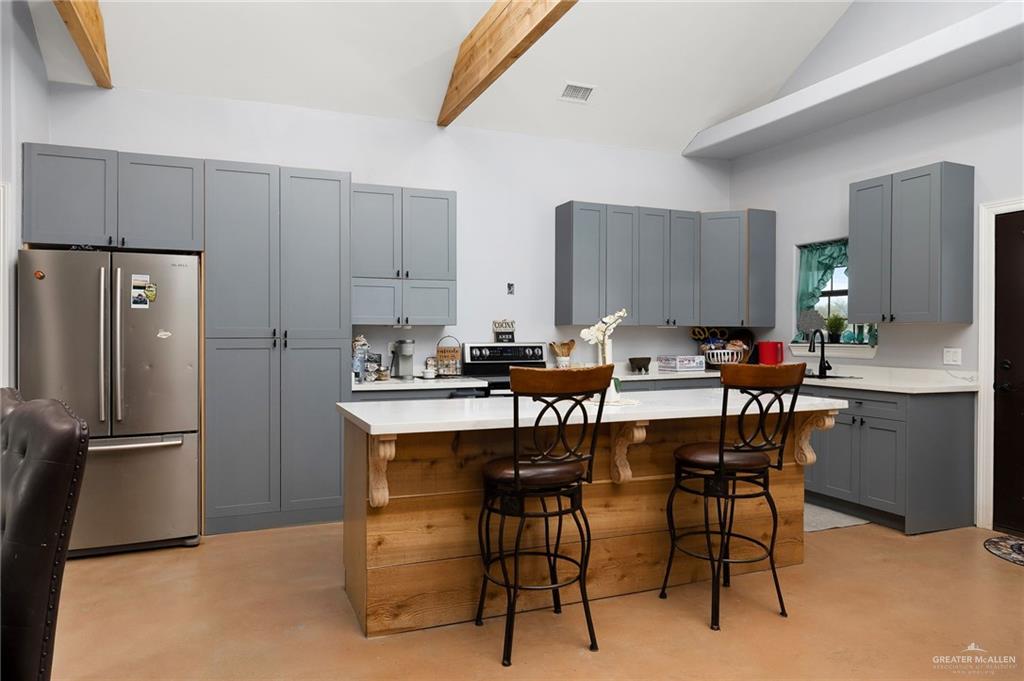 2991 North Us Highway Roma, TX 78584 - Photo 7 of 28 Kitchen with gray cabinetry, freestanding refrigerator, a kitchen island, a breakfast bar, and electric stove