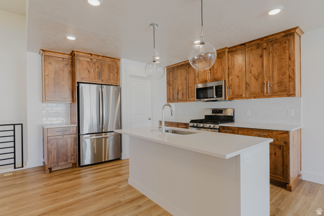 433 North 600 West Smithfield, UT 84335 - Photo 13 of 40 Kitchen featuring a central island with an undermount sink, stainless steel appliances, wood cabinetry, a tile backsplash, and wood-finish flooring
