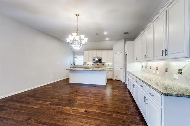 a large white kitchen with kitchen island a sink dishwasher a stove and a dining table with wooden floor