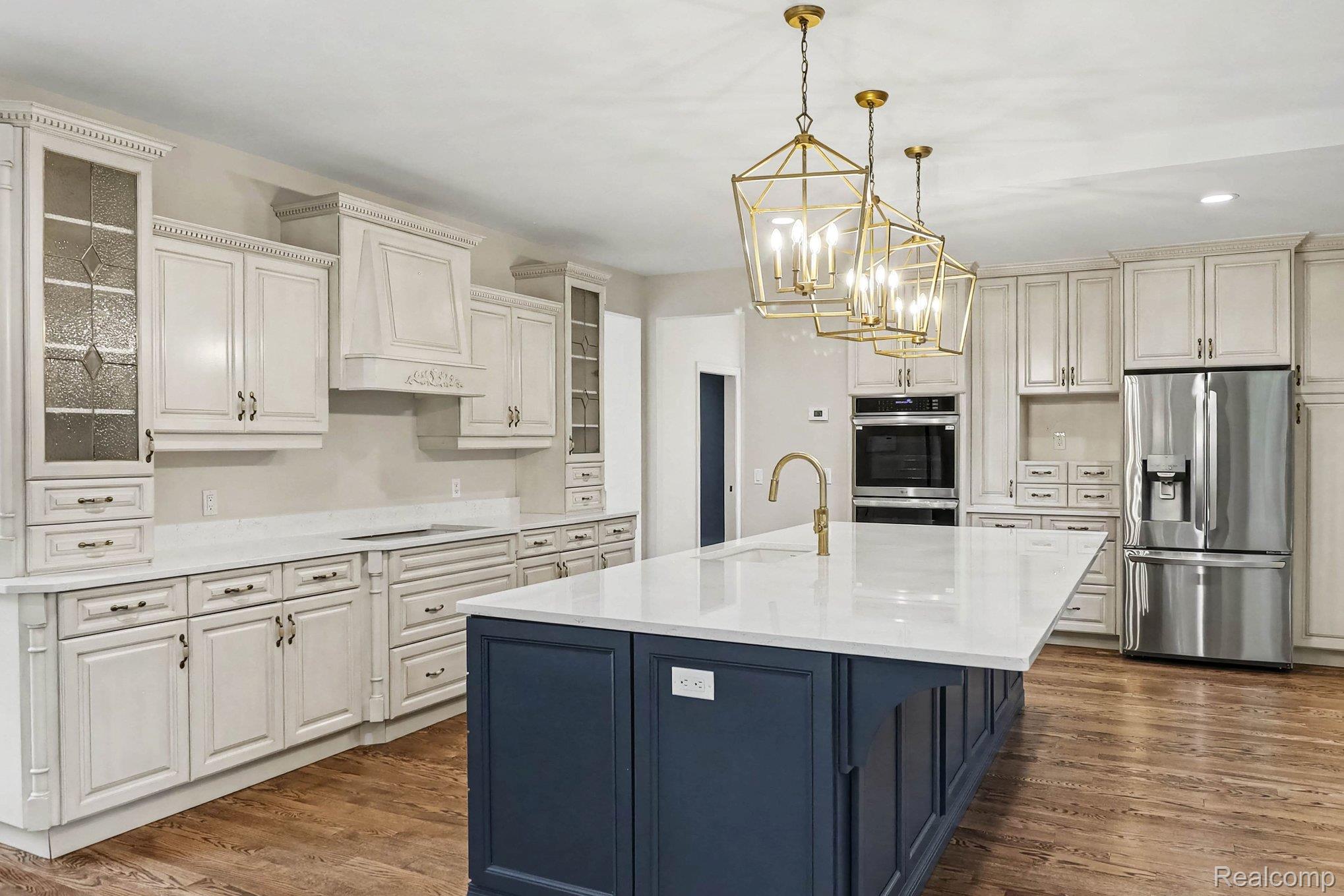 4875 Green Meadow Lane Rochester, MI 48306 - Photo 18 of 60 Expansive kitchen featuring a two-toned cabinet design, stainless steel appliances, a large central island with a sink, and decorative pendant lighting