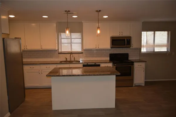 a kitchen with kitchen island granite countertop appliances cabinets and a sink