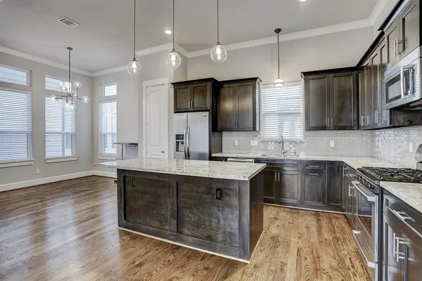 a large kitchen with stainless steel appliances a stove a sink dishwasher a refrigerator white cabinets wooden floor and a fireplace