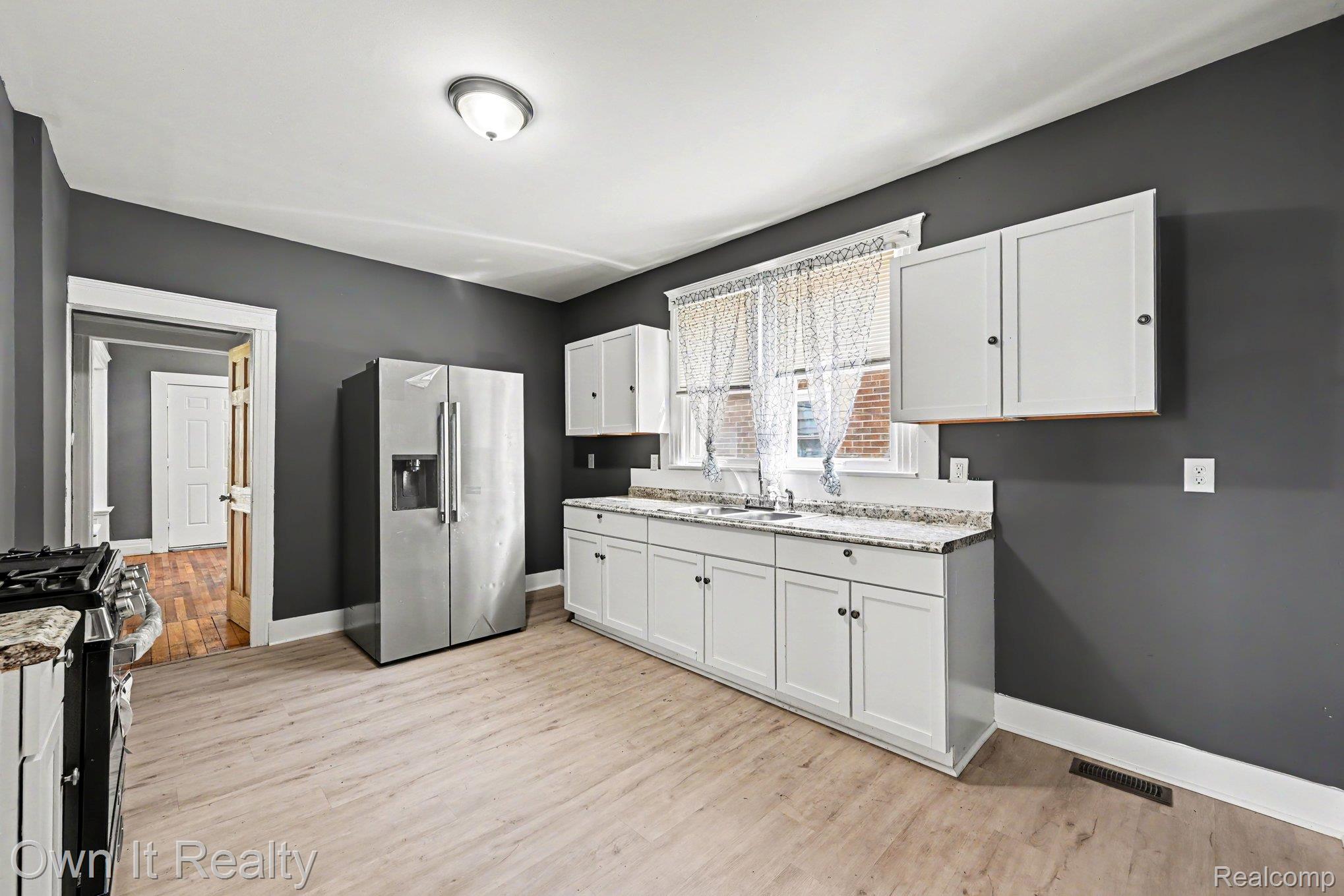 44 Maple Street River Rouge, MI 48218 - Photo 9 of 33 Light wood-finish flooring, white cabinetry, integrated sink, stainless steel French door refrigerator, and a stainless steel range with a griddle