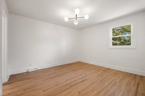 a view of an empty room with wooden floor and a chandelier fan