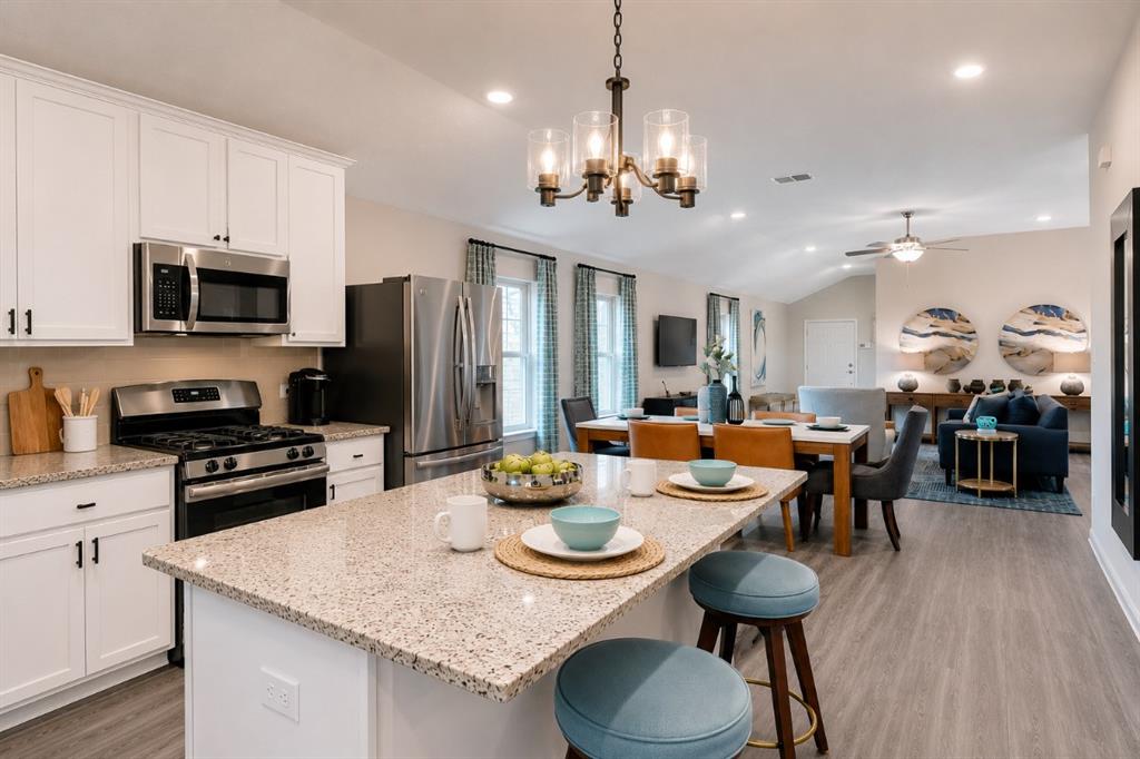 3344 Duncan Way Corinth, TX 76210 - Photo 8 of 38 Spacious open-concept interior featuring a kitchen island with granite-style countertops, stainless steel appliances, white cabinetry with dark hardware, and wood-finish flooring
