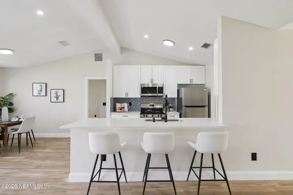 a kitchen with stainless steel appliances kitchen island granite countertop a dining table chairs and a refrigerator