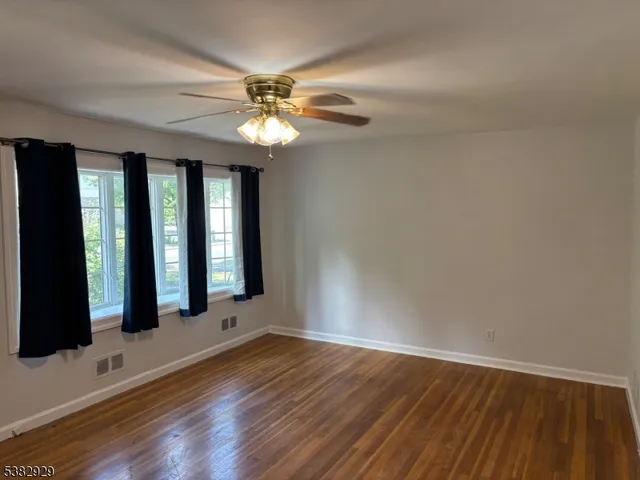 an empty room with wooden floor fan and windows
