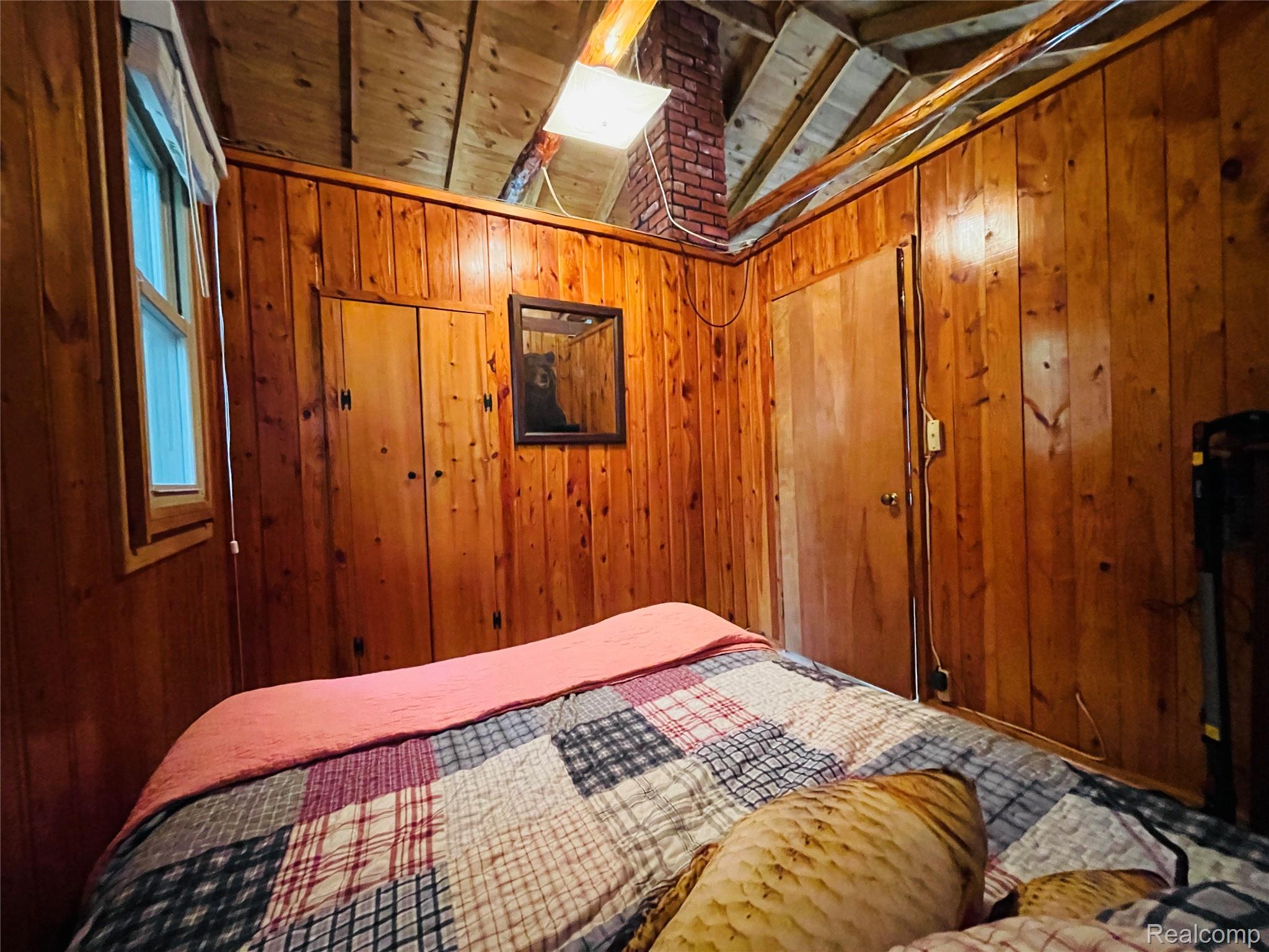 417 Ogemaw Road Rose City, MI 48654 - Photo 13 of 26 Wood-paneled room featuring a window, built-in closet, brick accent, and exposed ceiling beams