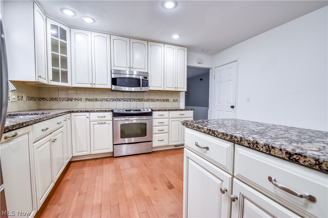 8242 Starburst Road Mentor, OH 44060 - Photo 5 of 37 Kitchen featuring white cabinetry with brushed nickel hardware, speckled countertops, stainless steel appliances, and wood-finish flooring