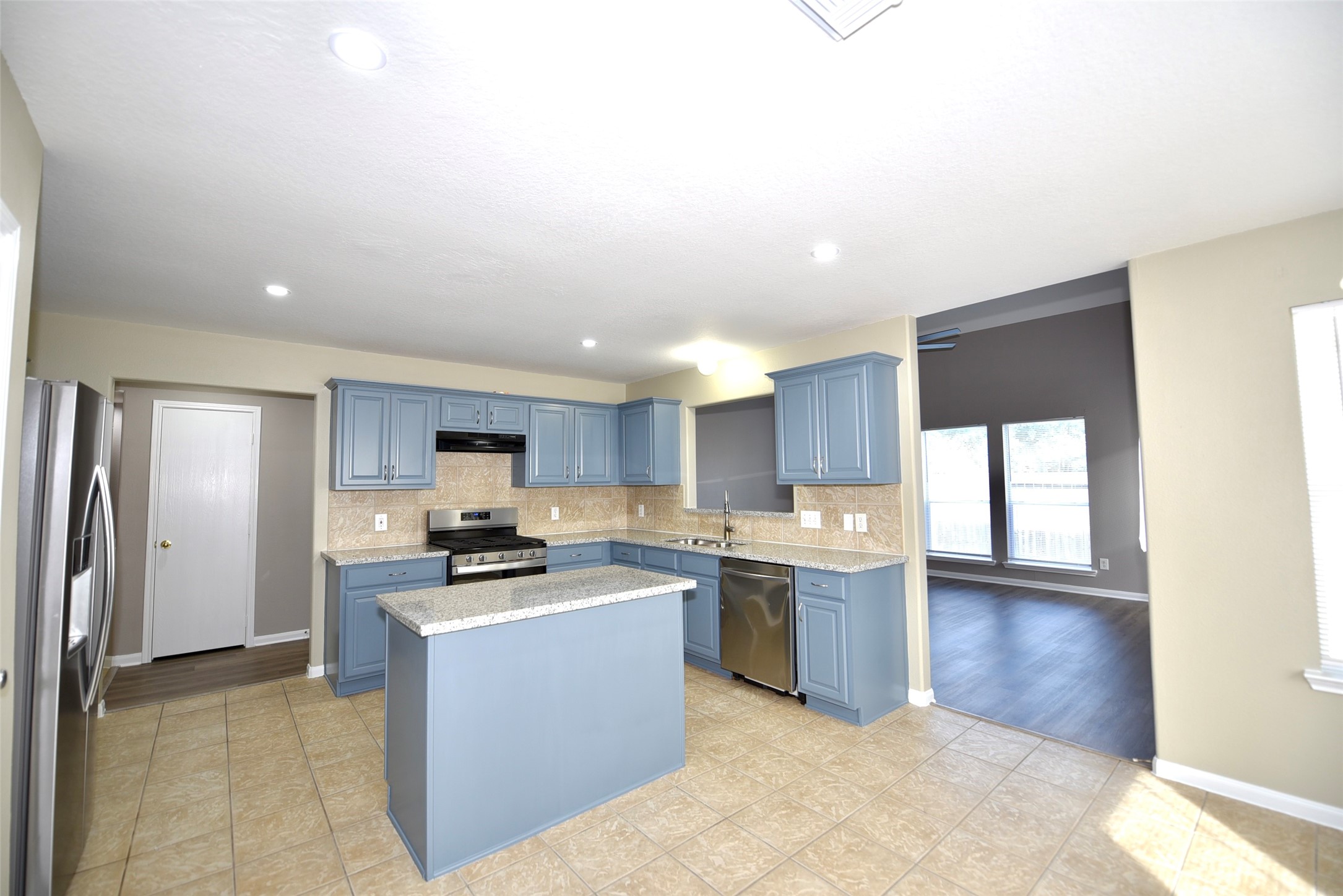 9611 Babbling Spring Court Tomball, TX 77375 - Photo 11 of 31 This modern kitchen features blue cabinetry, stainless steel appliances, and granite countertops. It opens up to a spacious living area with large windows, offering plenty of natural light and a view of the backyard.