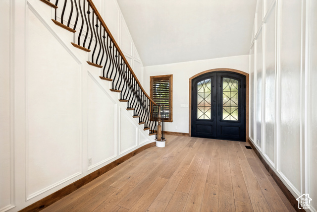 Welcoming bright and open grand entryway featuring a curved staircase with wrought iron balusters, light wood-finish flooring, and paneled walls.