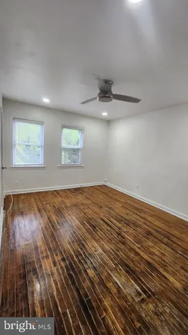 an empty room with wooden floor chandelier fan and windows