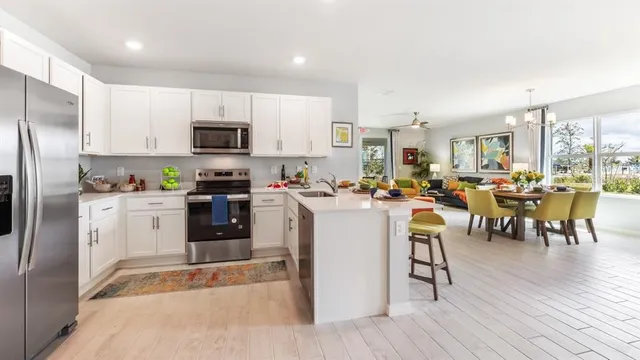 a kitchen with stainless steel appliances granite countertop a refrigerator a stove top oven a sink dishwasher a dining table and chairs with wooden floor
