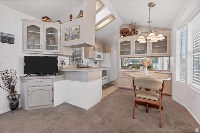 2990 East Riverside Drive, Unit 173 St. George, UT 84790 - Photo 4 of 38 Open-concept kitchen and dining area featuring vaulted ceilings, skylights, white cabinetry with glass-front uppers, and an integrated dining nook with bay windows