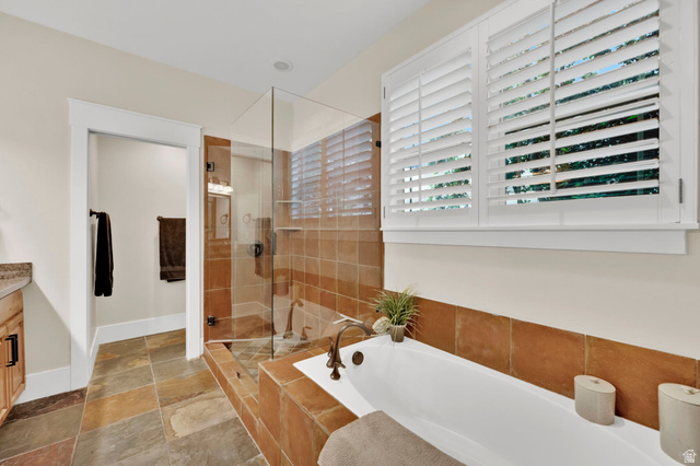 488 Mission Drive Midway, UT 84049 - Photo 25 of 35 Soaking tub with bronze fixtures, glass-enclosed shower, white plantation shutters, natural stone tile flooring, and a stone tile tub surround