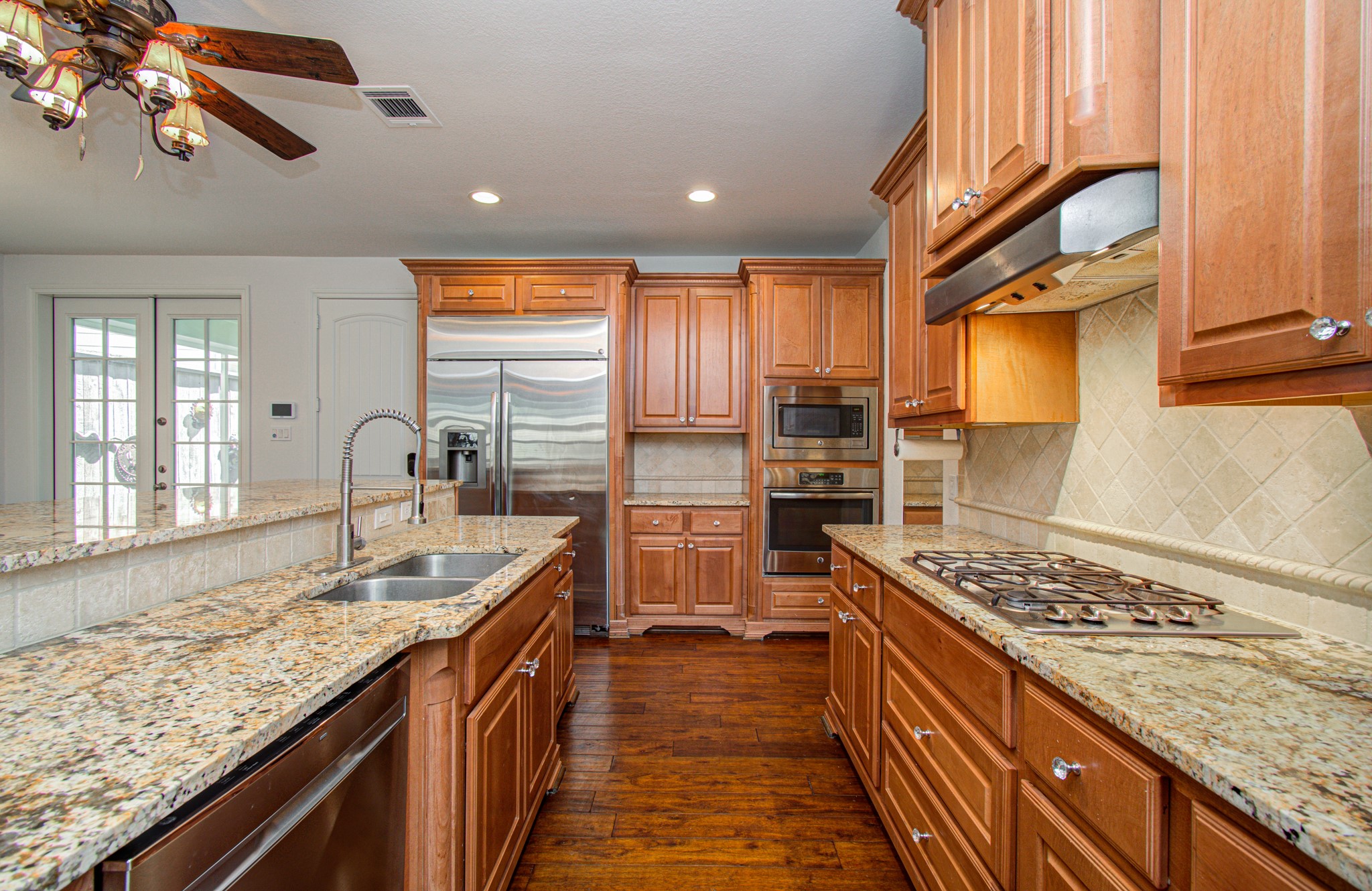 6621 North Main Street Houston, TX 77009 - Photo 12 of 41 This kitchen features warm wood cabinetry, granite countertops, and stainless steel appliances, including a built-in oven and gas cooktop. It has a central island with a sink and ample storage, complemented by a classic tile backsplash and hardwood floors.