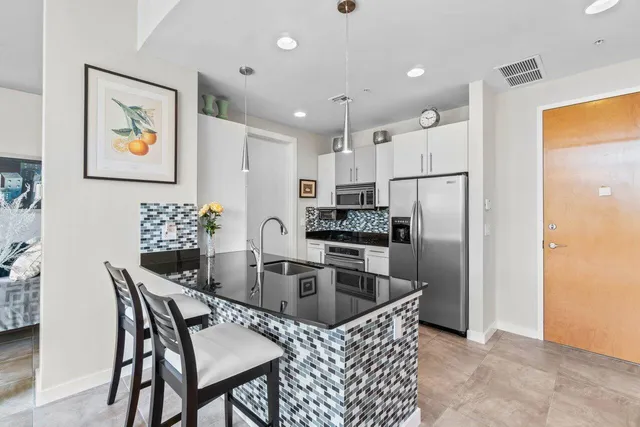 a kitchen with stainless steel appliances granite countertop a refrigerator a sink a stove a dining table and chairs with wooden floor