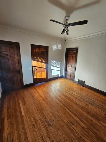 an empty room with wooden floor chandelier fan and windows