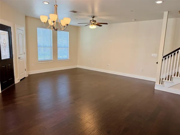 an empty room with wooden floor chandelier fan and windows