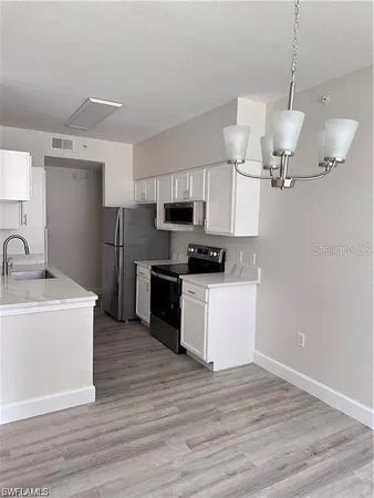 a kitchen with stainless steel appliances granite countertop a sink a microwave oven a refrigerator and white cabinets with wooden floor