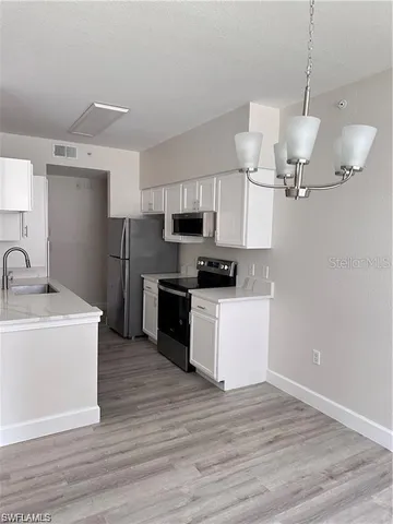 a kitchen with stainless steel appliances granite countertop a sink a microwave oven a refrigerator and white cabinets with wooden floor