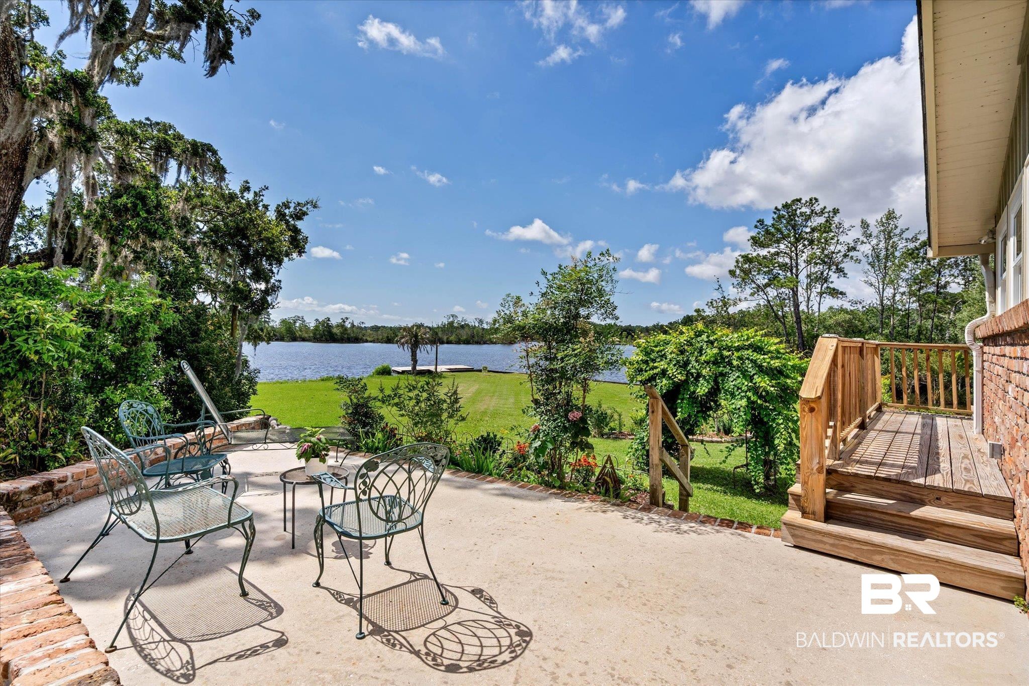 3801 Point Road Mobile, AL 36619 - Photo 32 of 55 Waterfront backyard featuring a concrete patio with a brick knee wall, manicured lawn, mature trees, and a private wooden dock