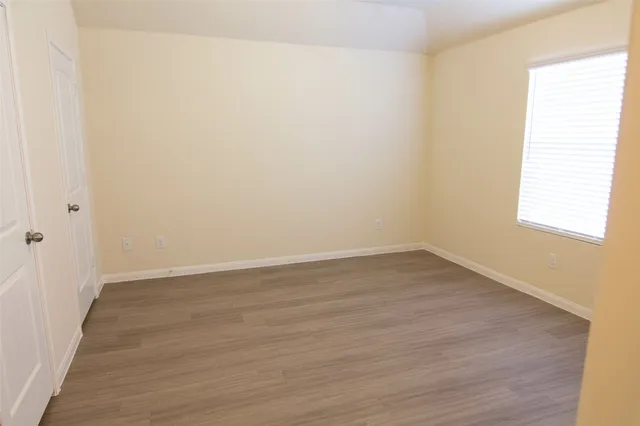 a view of an empty room with wooden floor and a window