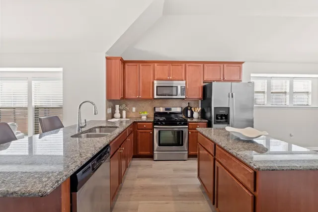 a kitchen with stainless steel appliances granite countertop a refrigerator a sink dishwasher a stove with wooden cabinets and floor