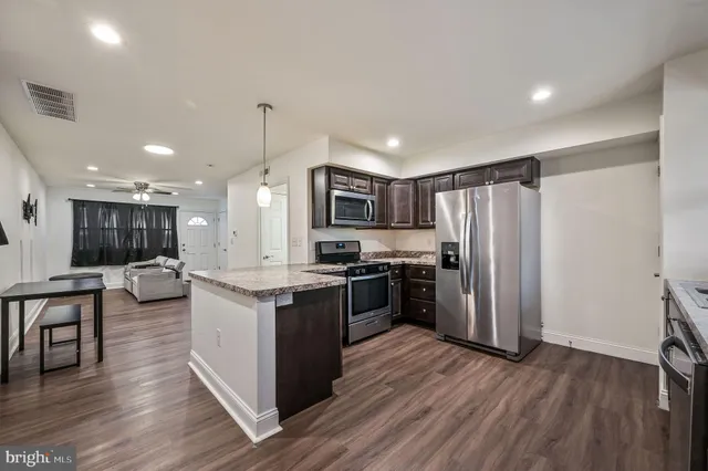 a kitchen with stainless steel appliances granite countertop a refrigerator a stove top oven a sink dishwasher and a refrigerator with wooden floor
