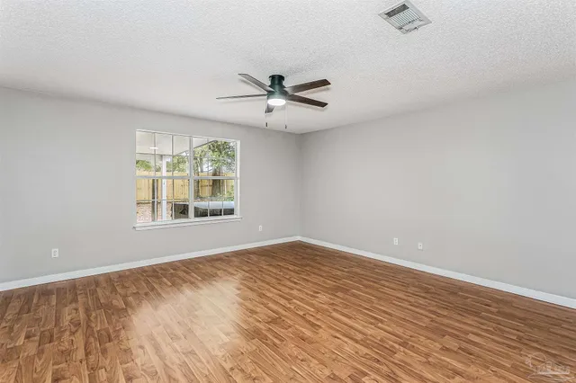 an empty room with wooden floor ceiling fan and windows