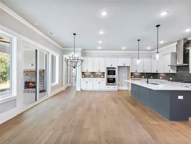 a large kitchen with kitchen island a refrigerator a stove a oven a large island with wooden floor and ceiling cabinets