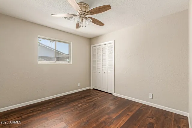 an empty room with wooden floor chandelier fan and windows