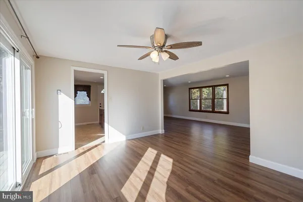 a view of a livingroom with wooden floor a ceiling fan and windows