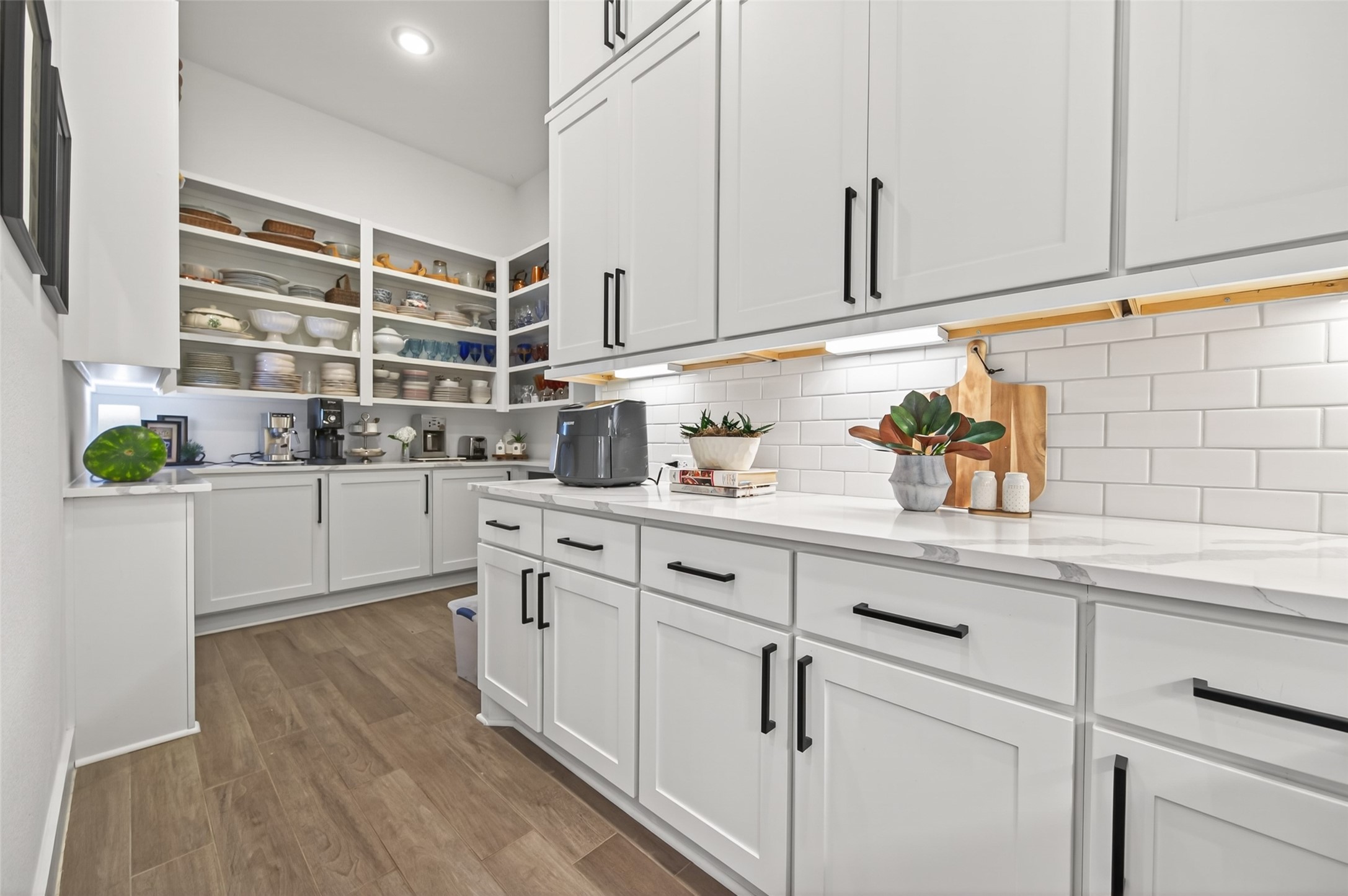 29612 Fulshear Lake Trace Fulshear, TX 77406 - Photo 24 of 48 This photo showcases a modern, well-organized pantry with ample storage. It features white cabinetry, open shelves, and sleek countertops, complemented by a subway tile backsplash. The space is bright and functional, ideal for efficient kitchen organization. Check beautiful countertop!